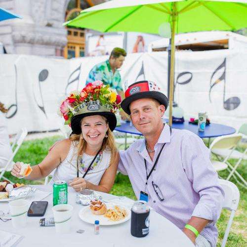 people sitting with fun hats at tables outside with colorful umbrellas